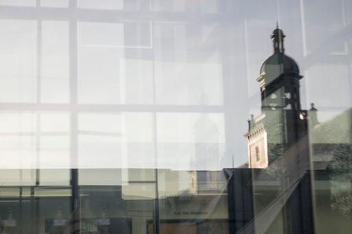 Photo by Katherine Turner. Reflection of the Denny Hall bell tower in the windows of PACCAR Hall Business School.