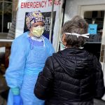 A medical professional in personal protective equipment talks to a patient in a mask outside a triage tent for evaluating potential COVID-19 cases